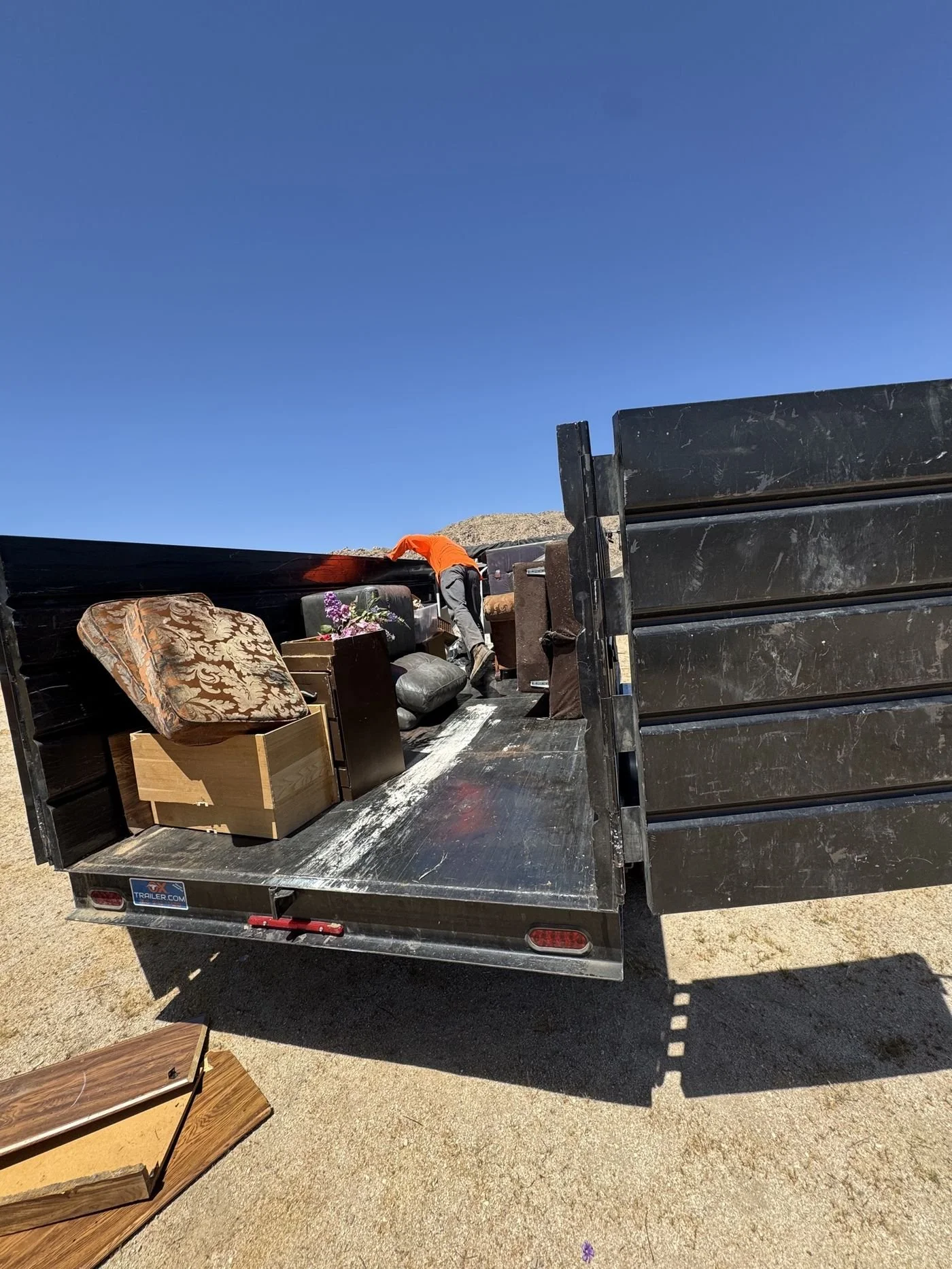 Black Carson high-side dump trailer with the tailgate open, loaded with furniture, dressers and a couch while a worker loads more inside
