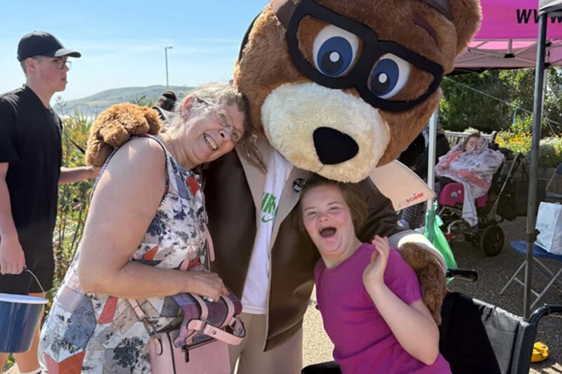 Bear mascot posing for a photo with a woman and a girl in a wheelchair at the Airbourne event