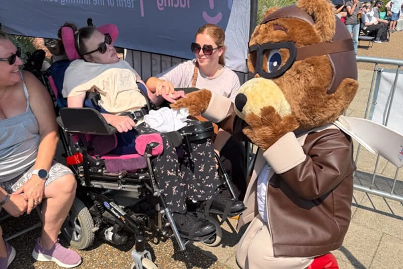 Family with a girl in a wheelchair meeting the Forward Facing bear mascot beside the event banner
