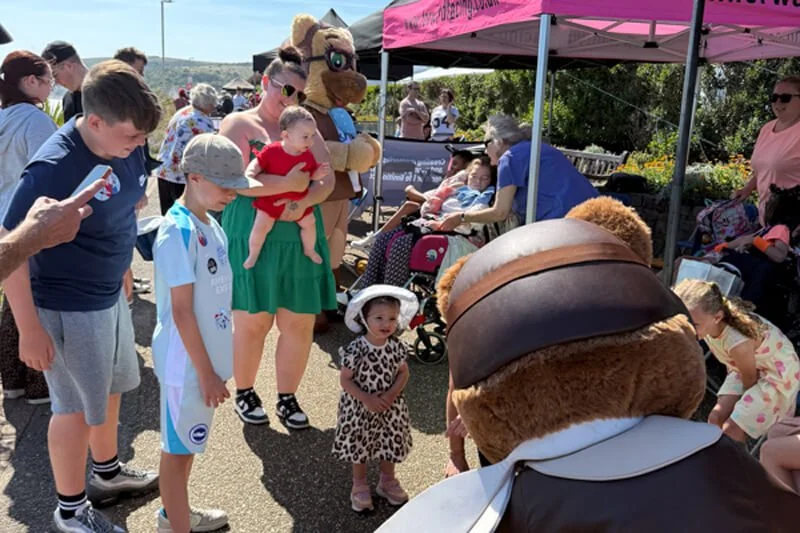 Children and families queuing to meet the Forward Facing bear mascot by the event gazebo
