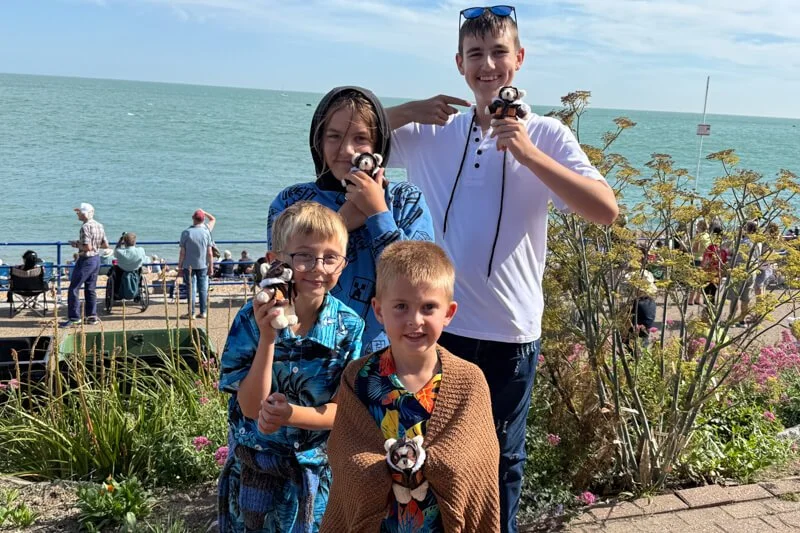 Group of boys by the sea smiling and holding small teddy bears at the airshow