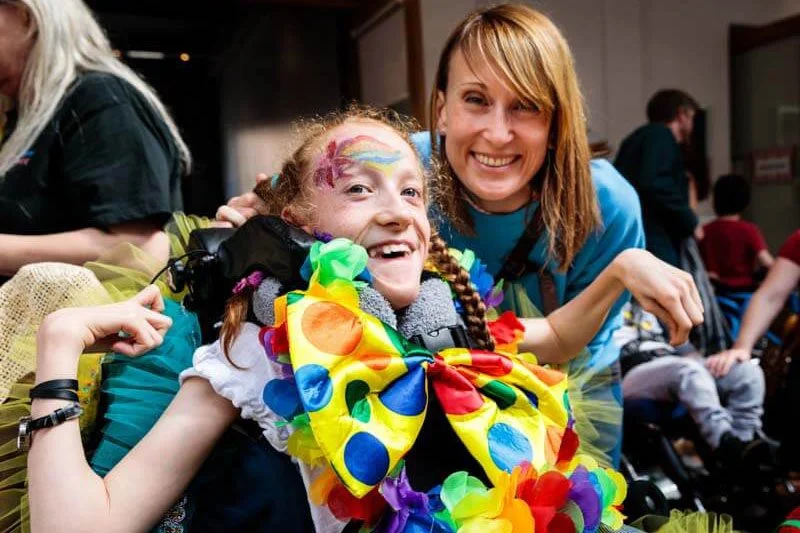 A very happy girl in a wheelchair wearing a costume bow tie with big spots