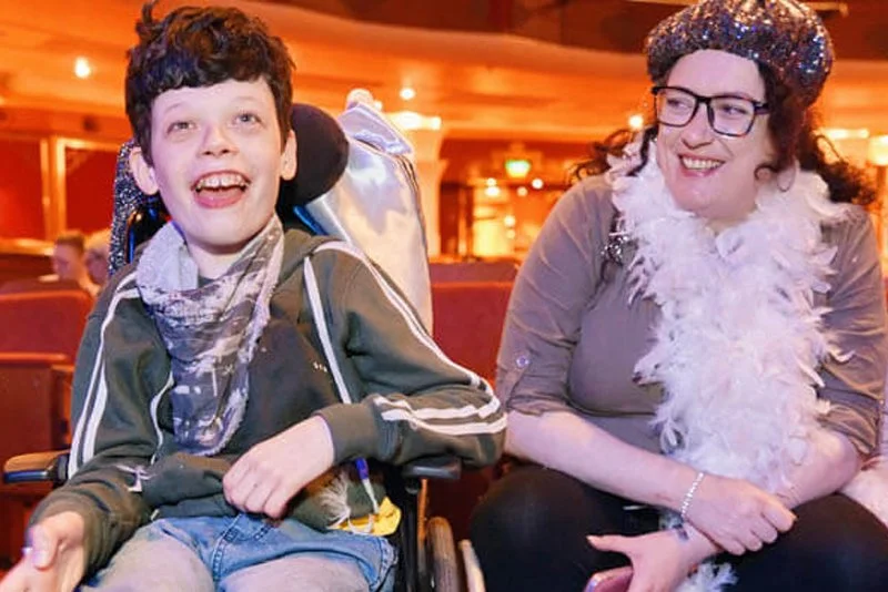 A boy in a wheelchair sits in the audience with a woman and another girl at Memory Making Day
