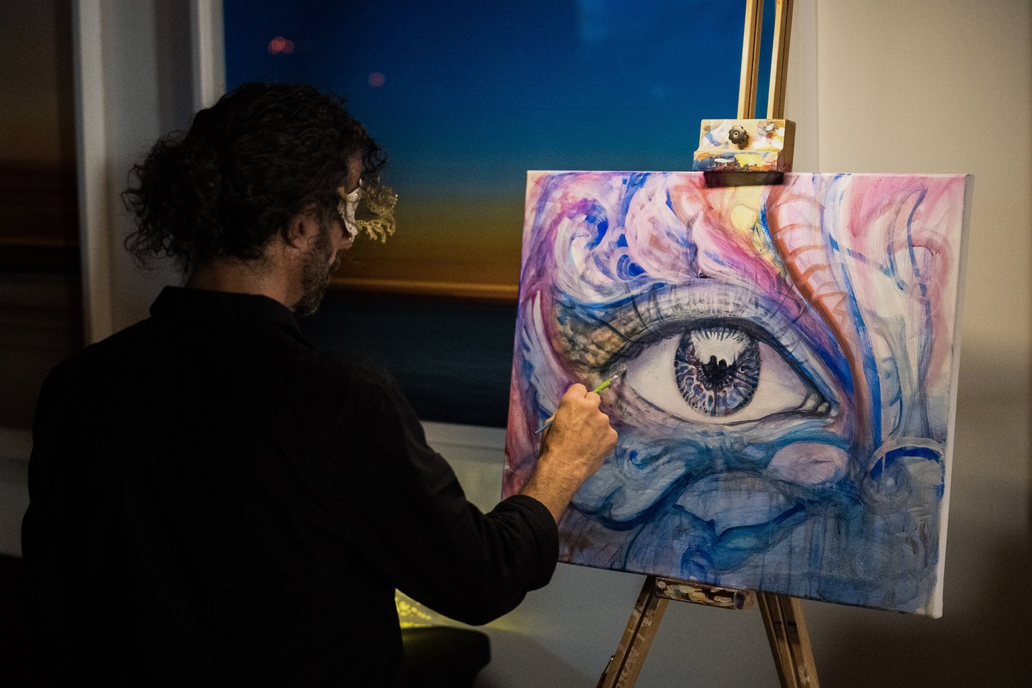 Artist painting a colorful eye on a canvas at Arcana.