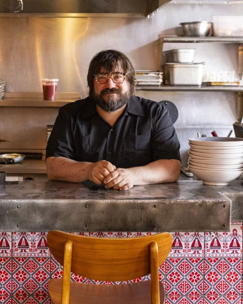 Chef Bo Porytko Molotov seated behind a restaurant counter in a commercial kitchen.