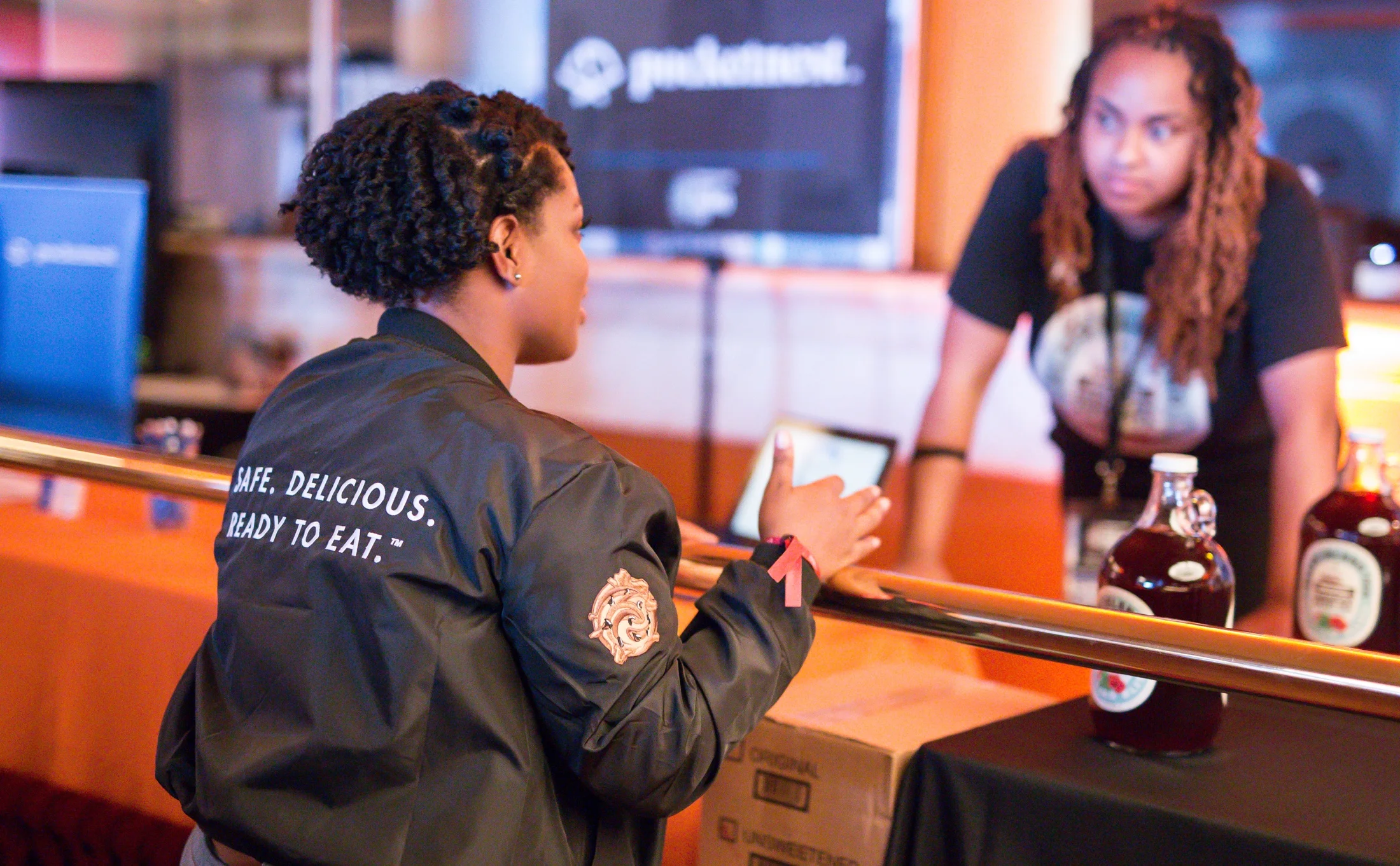 Woman wearing a Detroit Dough jacket printed with Safe. Delicious. Ready to Eat. while talking with a coworker at an event