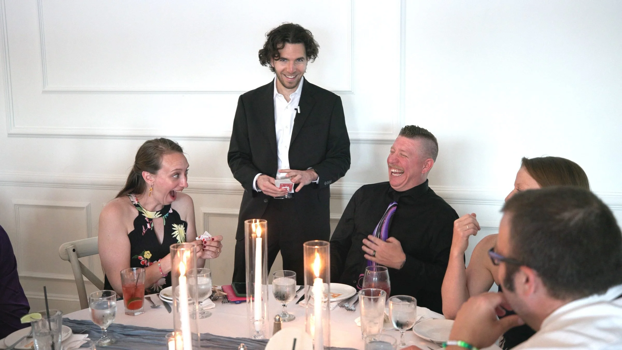 Guests laughing and reacting to close-up card magic during a dinner reception