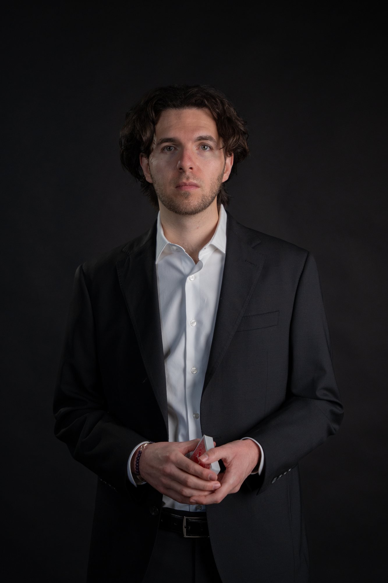 Ben Travelyn, Rhode Island and Boston magician, holding a deck of cards in a dark suit