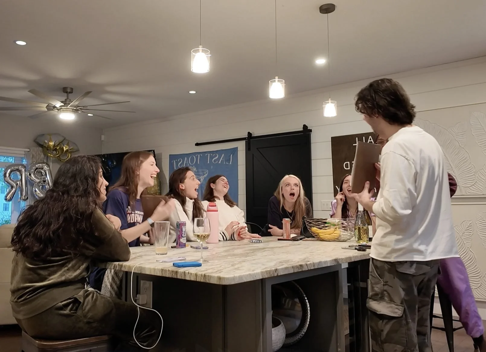 Group of guests laughing and gasping at close-up magic around a kitchen island
