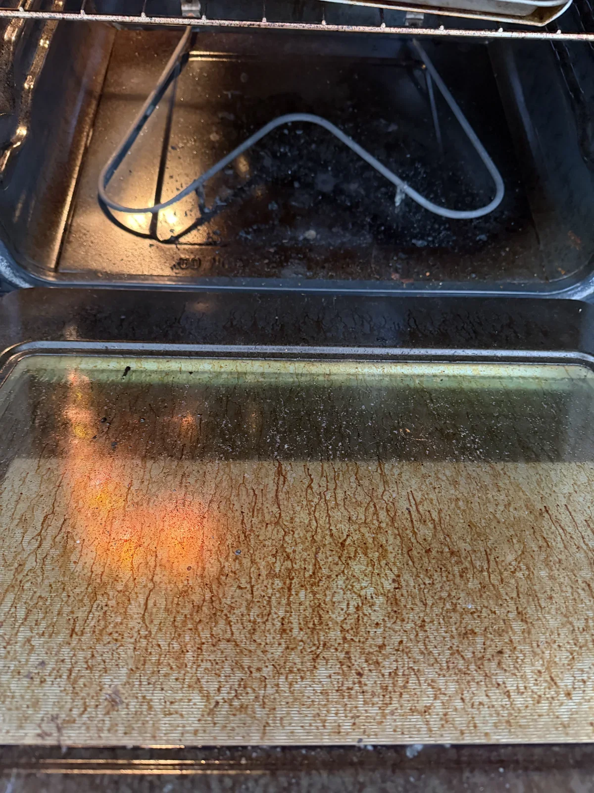Electric oven with dark baked-on residue across the bottom and door glass before cleaning