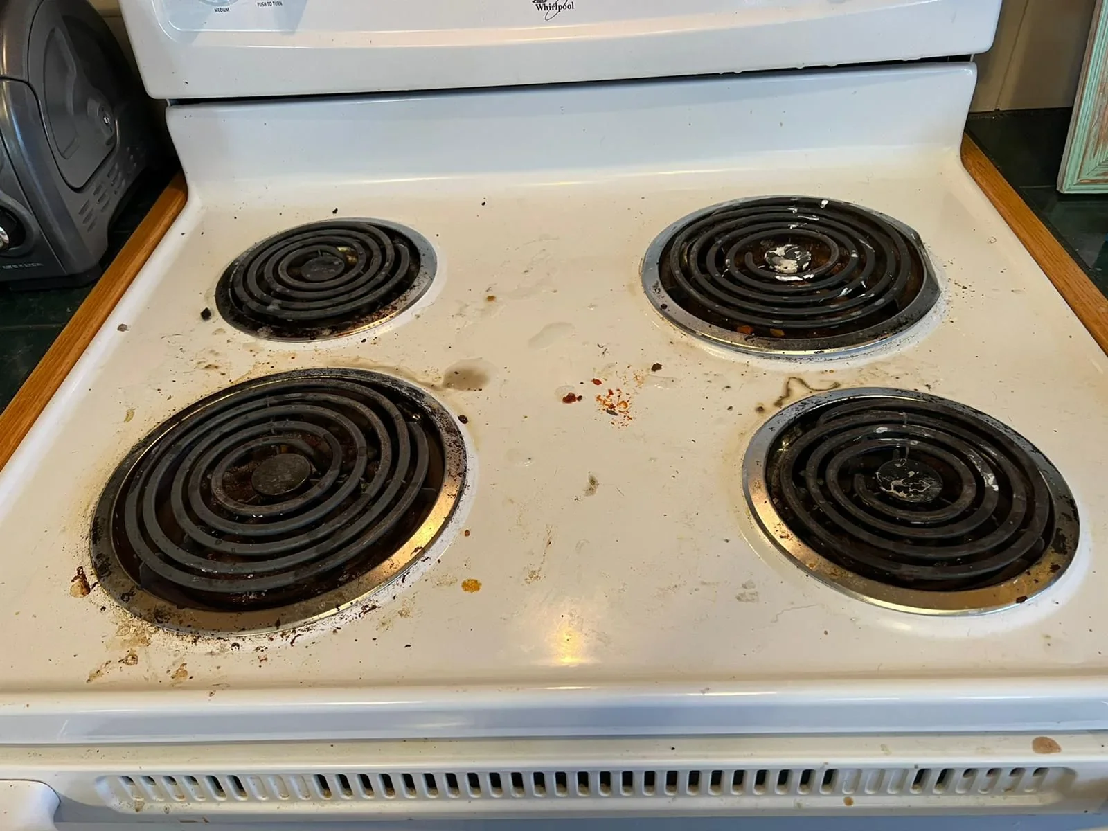 White electric stovetop with food debris and brown cooking residue around the burners before cleaning