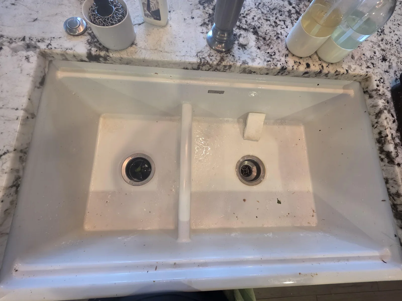 White double-basin kitchen sink with debris and residue before cleaning