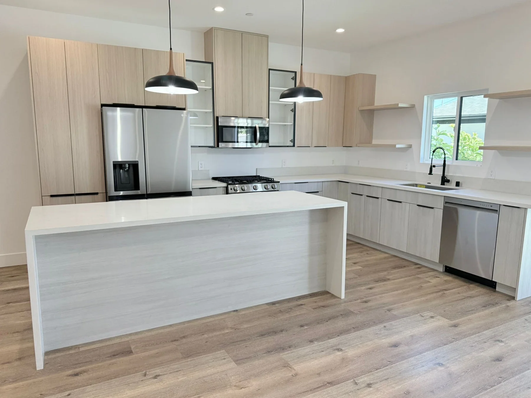 Modern kitchen with warm wood cabinetry, a white waterfall peninsula and black pendant lights