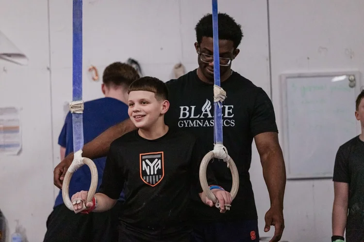 Smiling boy holding gymnastics rings as a Blaze coach guides him