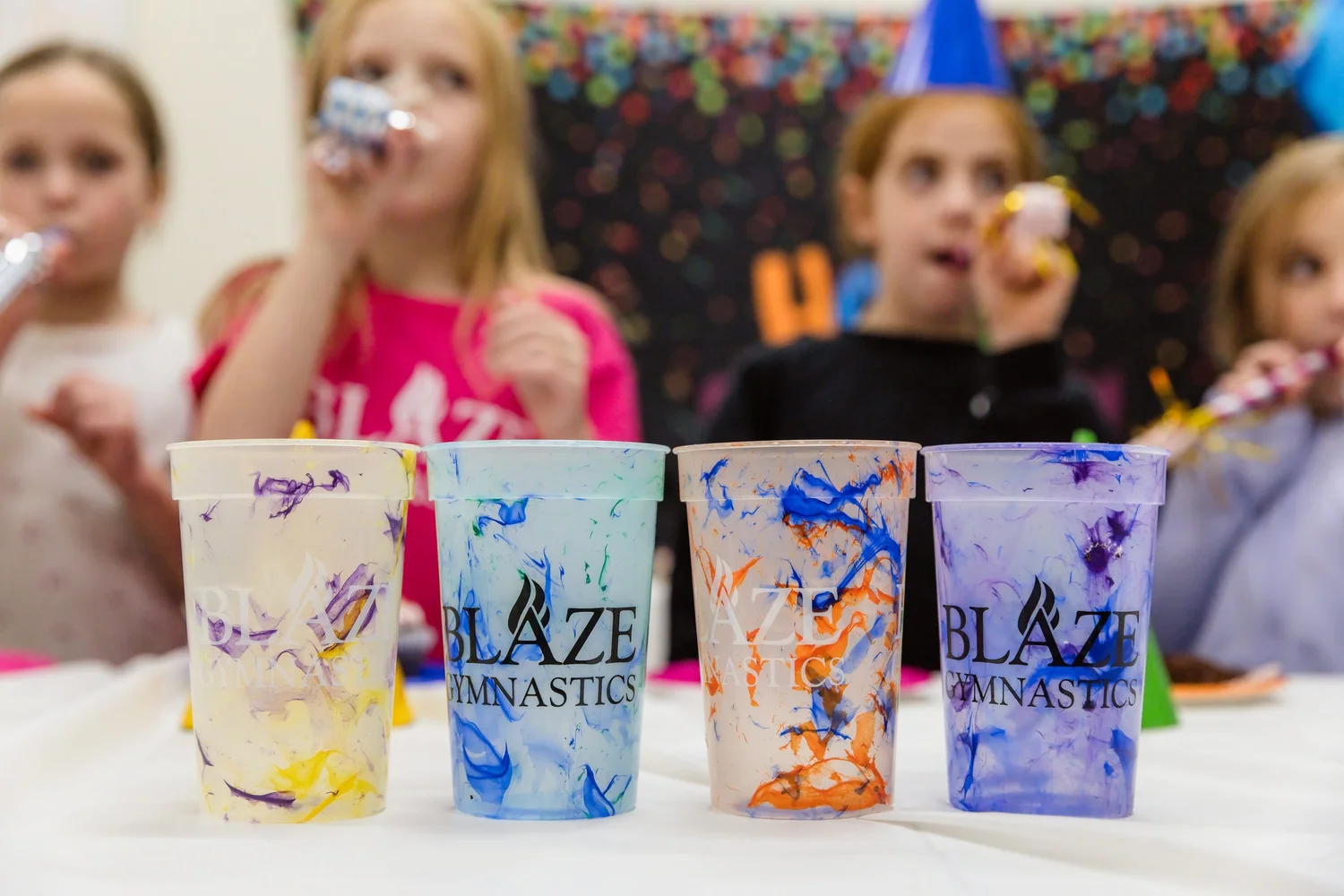 Colorful Blaze Gymnastics party cups lined up on a party table with kids celebrating in the background.