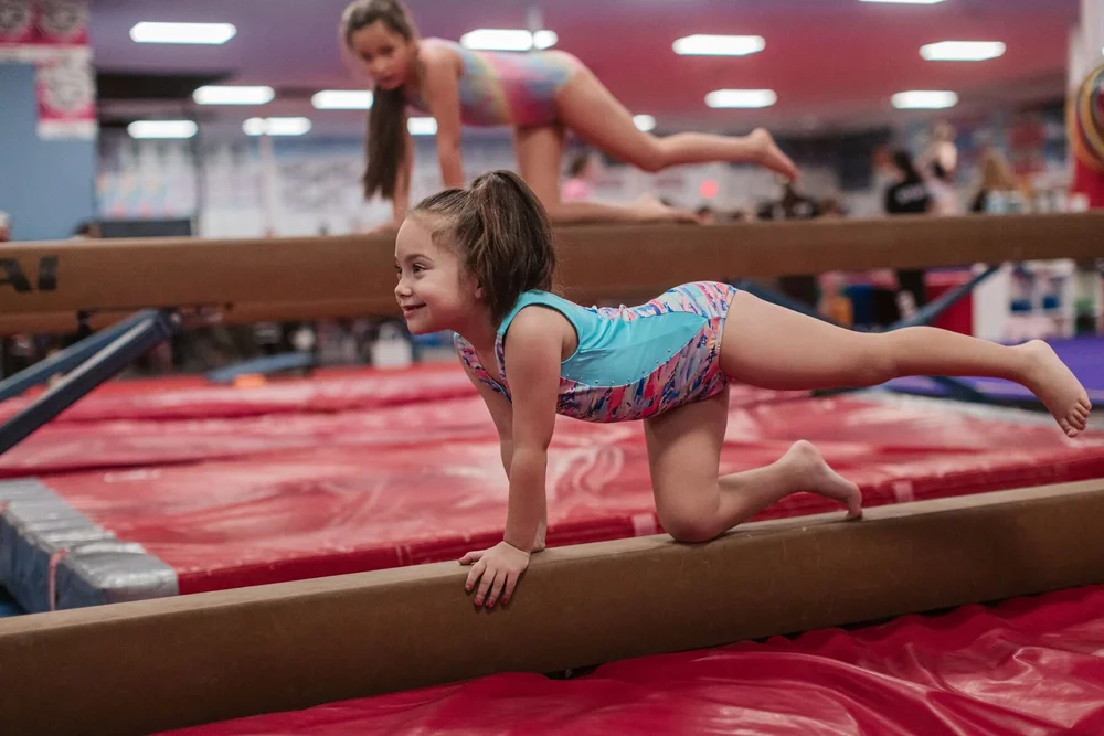 Smiling young gymnast crawling along a low balance beam during a beginner class at Blaze Gymnastics
