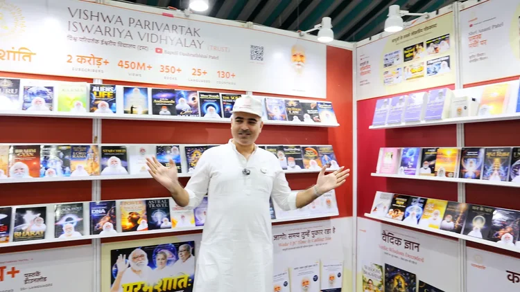 A volunteer in white welcomes visitors at the Vishwa Parivartak Iswariya Vidhyalay stall