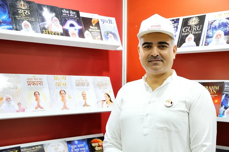 A volunteer in a white Param Shanti cap stands beside bookshelves