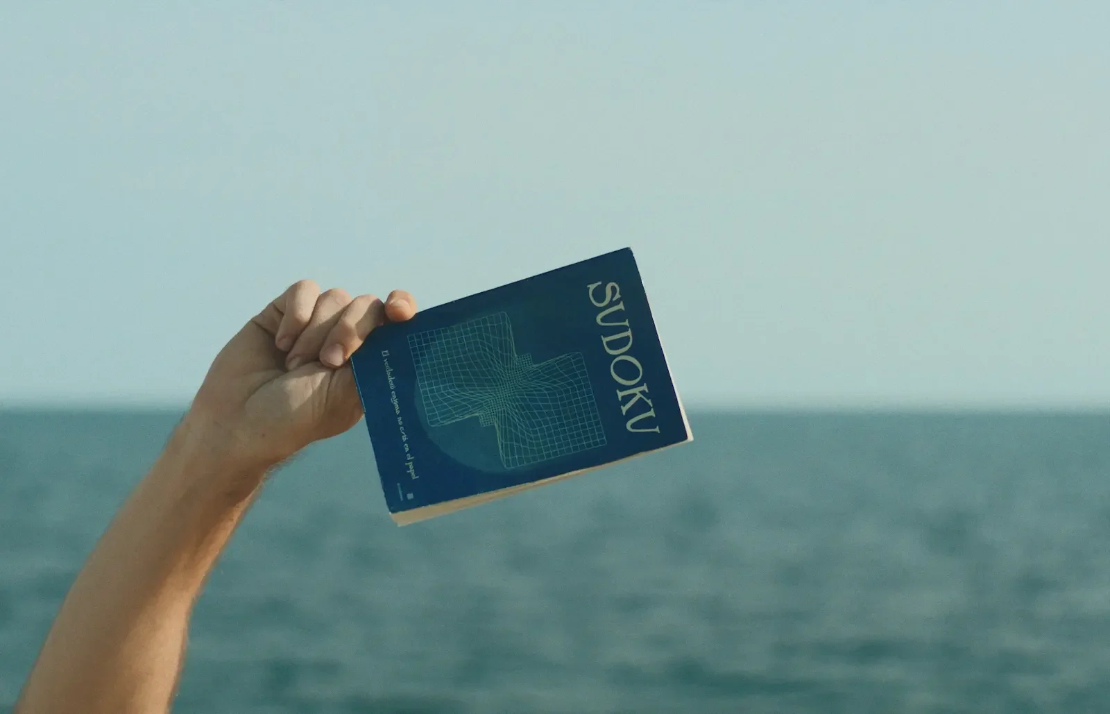Una mano sostiene el libro de sudoku frente al Mediterráneo.