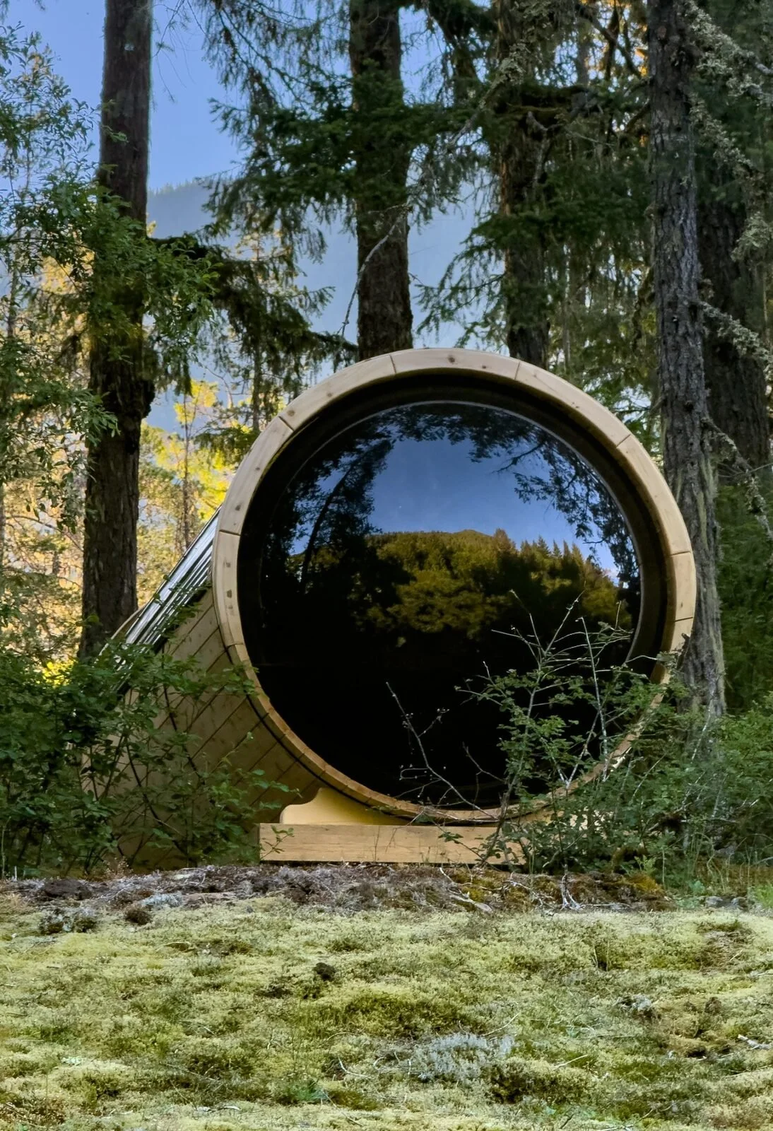 Round picture window on a cedar glamping barrel surrounded by old-growth forest