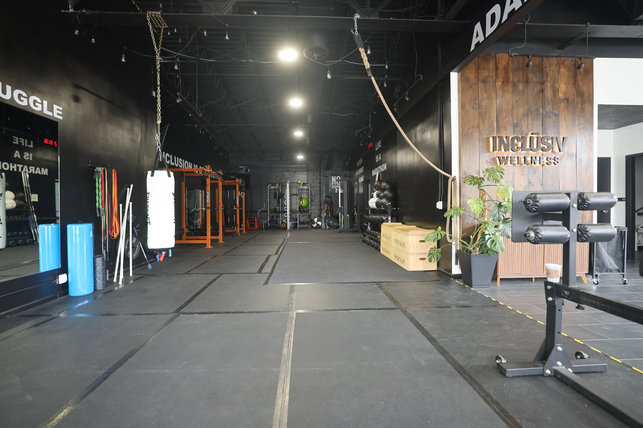 The open INCLŪSIV Wellness gym floor with the lit INCLŪSIV sign