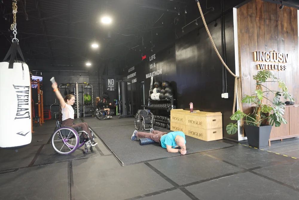 A member in a wheelchair raising her arm in celebration beside the heavy bag