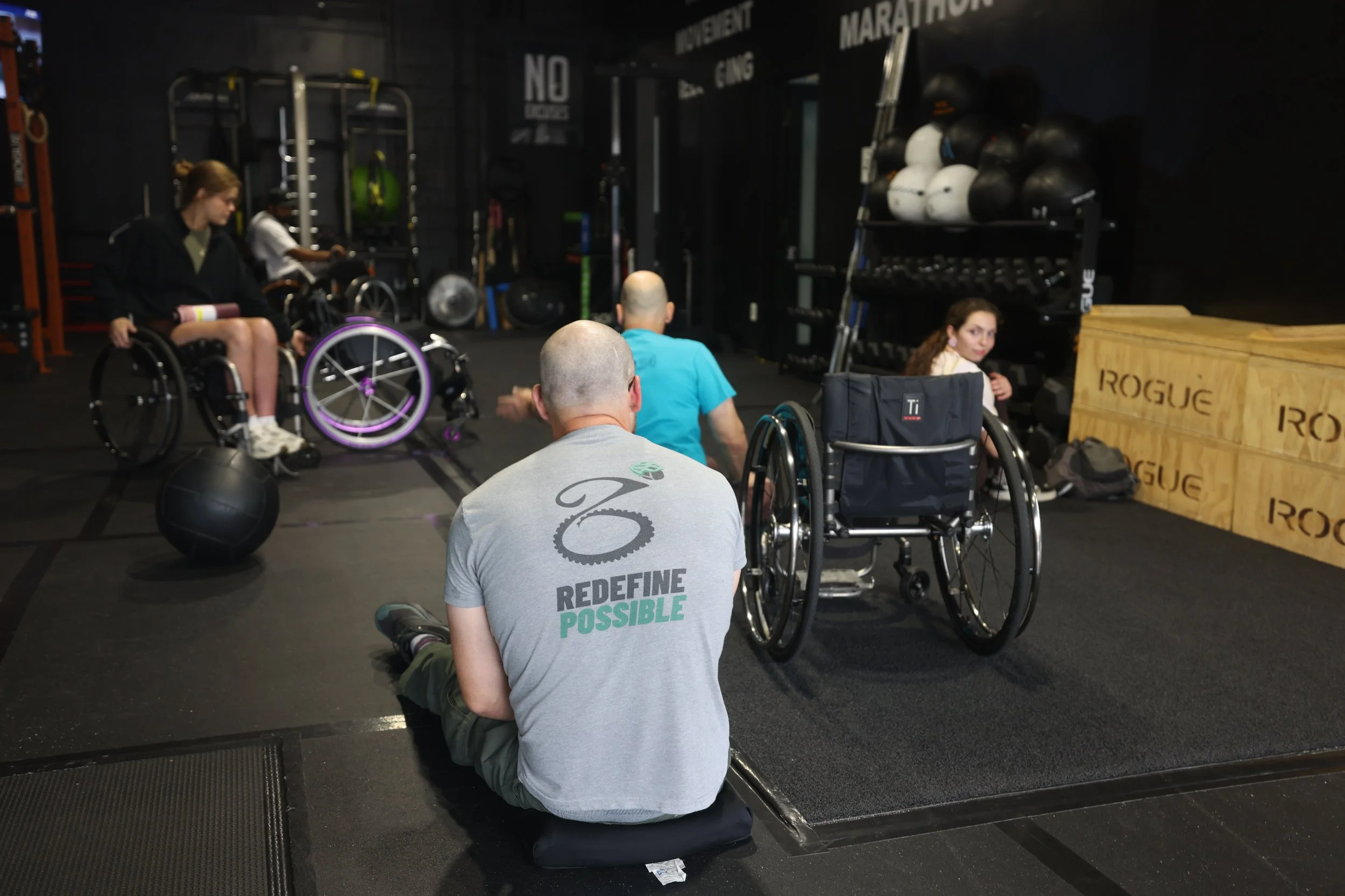 Members training together on the floor at INCLŪSIV Wellness, one wearing a Redefine Possible shirt