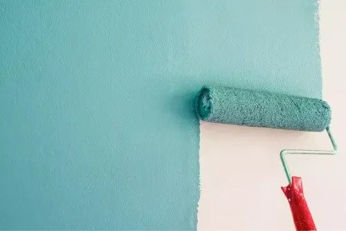 Paint roller applying teal paint on a wall
