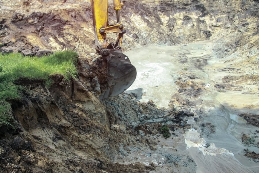 Excavator removing contaminated soil as part of a land remediation strategy and site verification process.