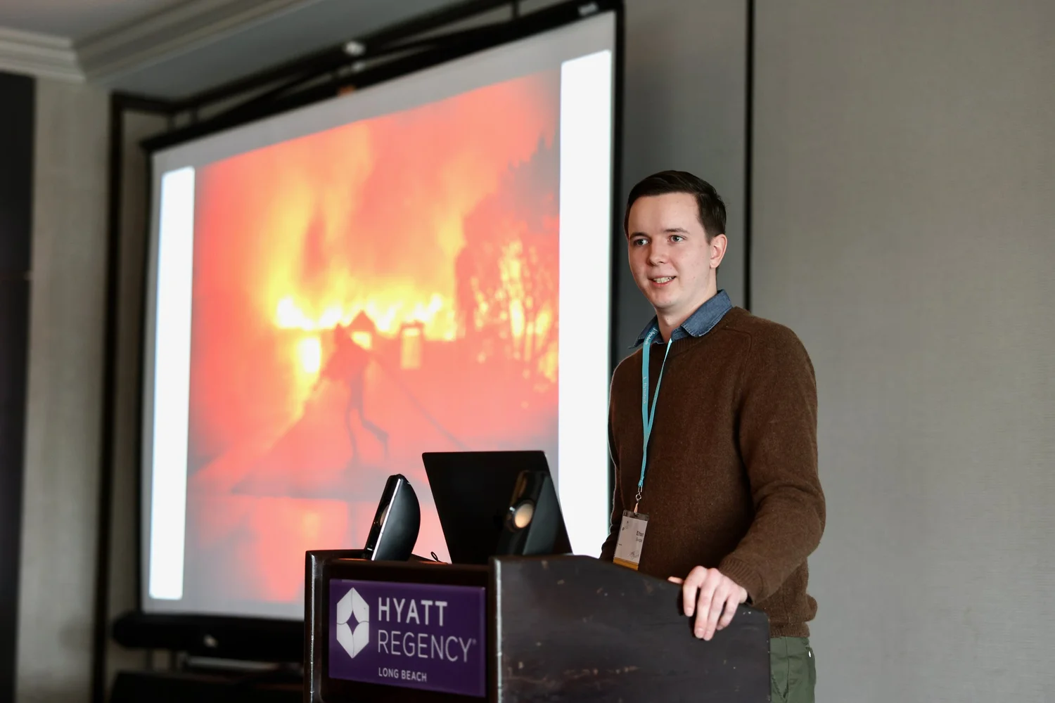 A speaker presents wildfire photographs at a lectern.