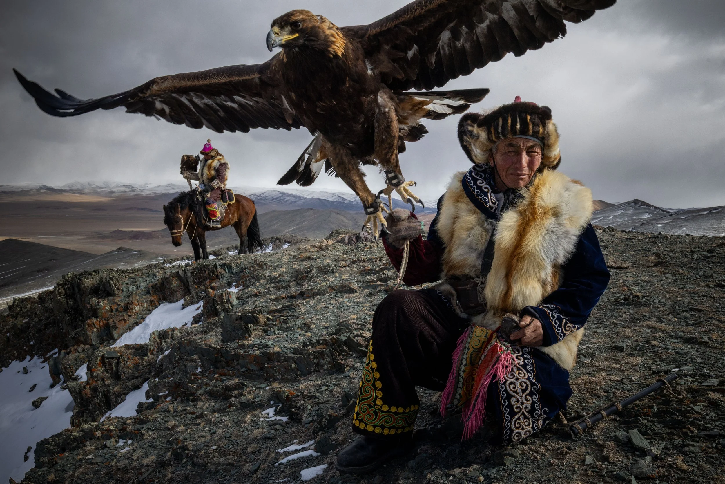 A golden eagle spreads its wings above a seated hunter in the mountains of Mongolia.
