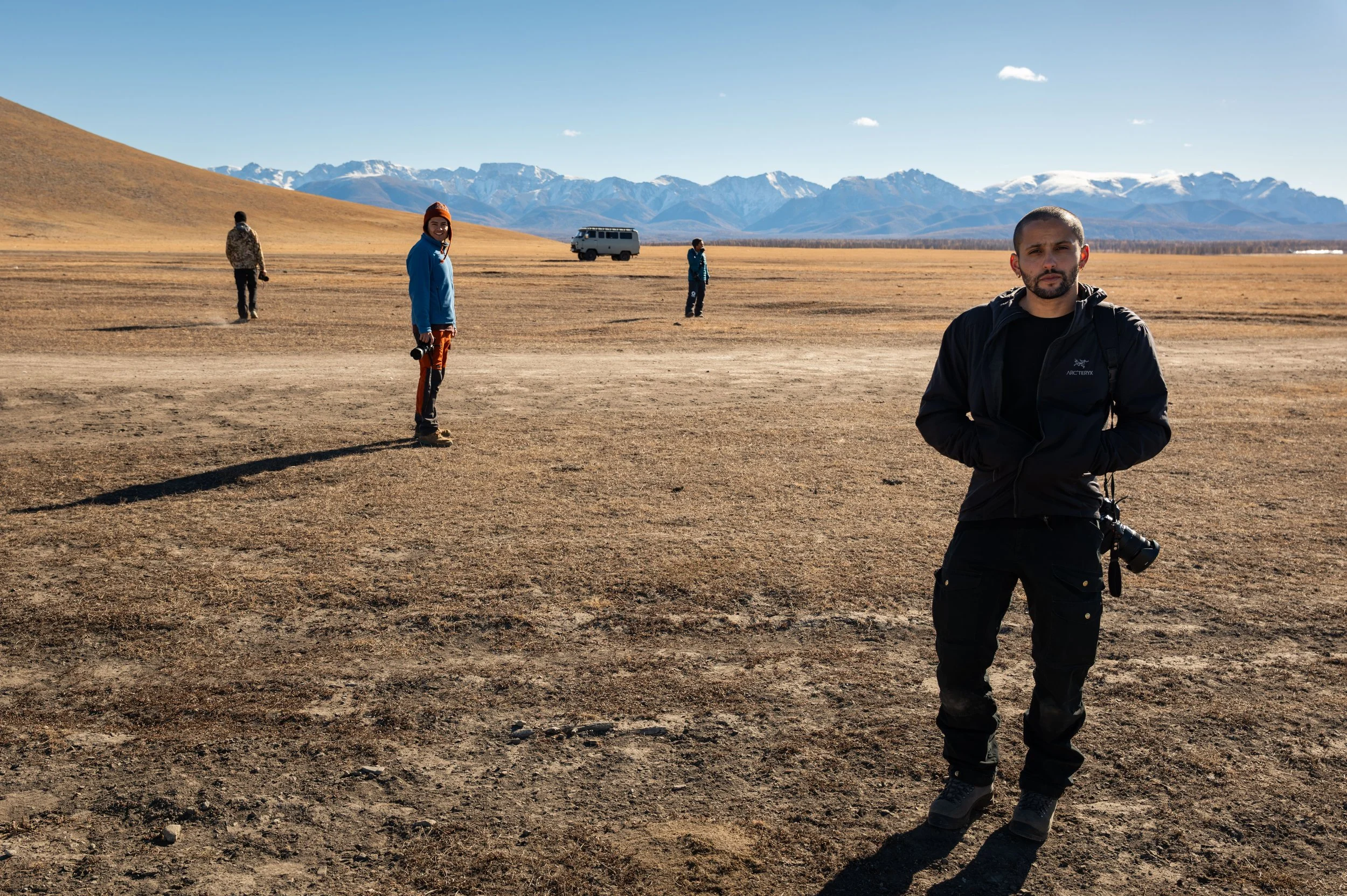 Photographers working across an open landscape beneath snow-capped mountains.