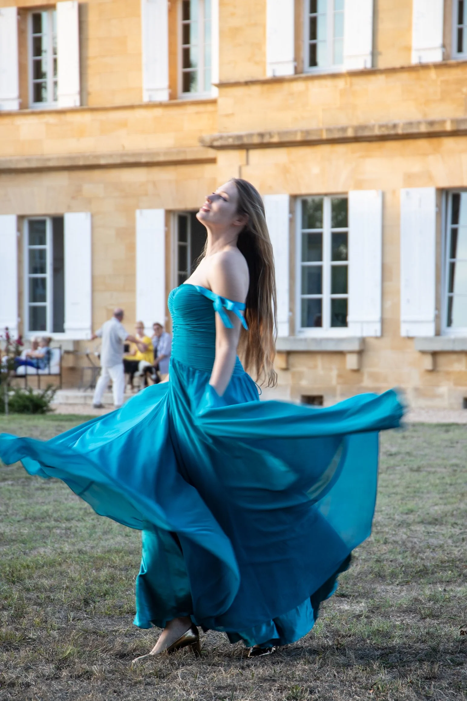 A young singer turning in a flowing turquoise gown outside Château de Monboucher