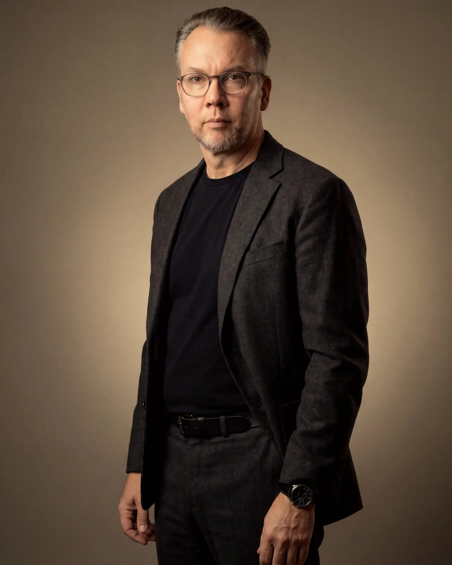 Full-length studio portrait in a charcoal jacket against a warm backdrop