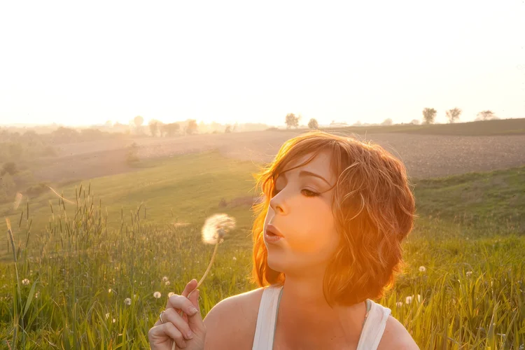 Young woman blowing a dandelion