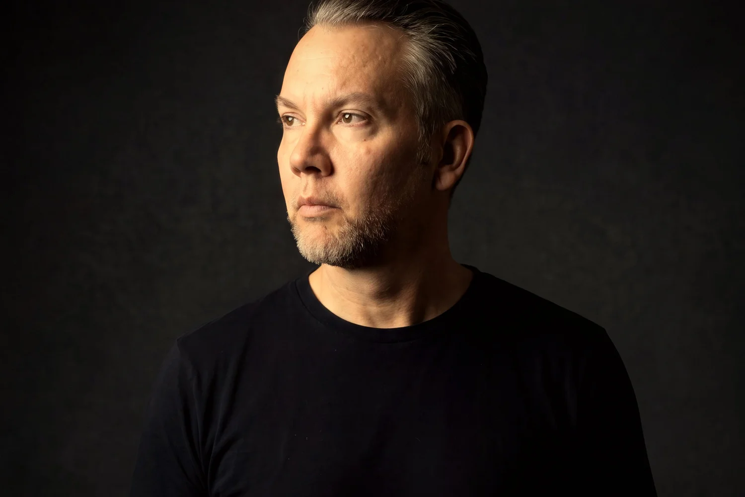 Studio portrait in profile, looking off to the left, dark backdrop
