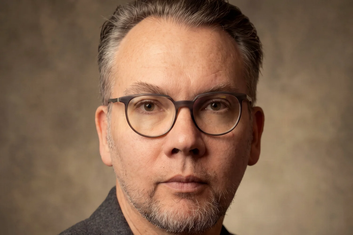 Close studio portrait with glasses, warm mottled backdrop