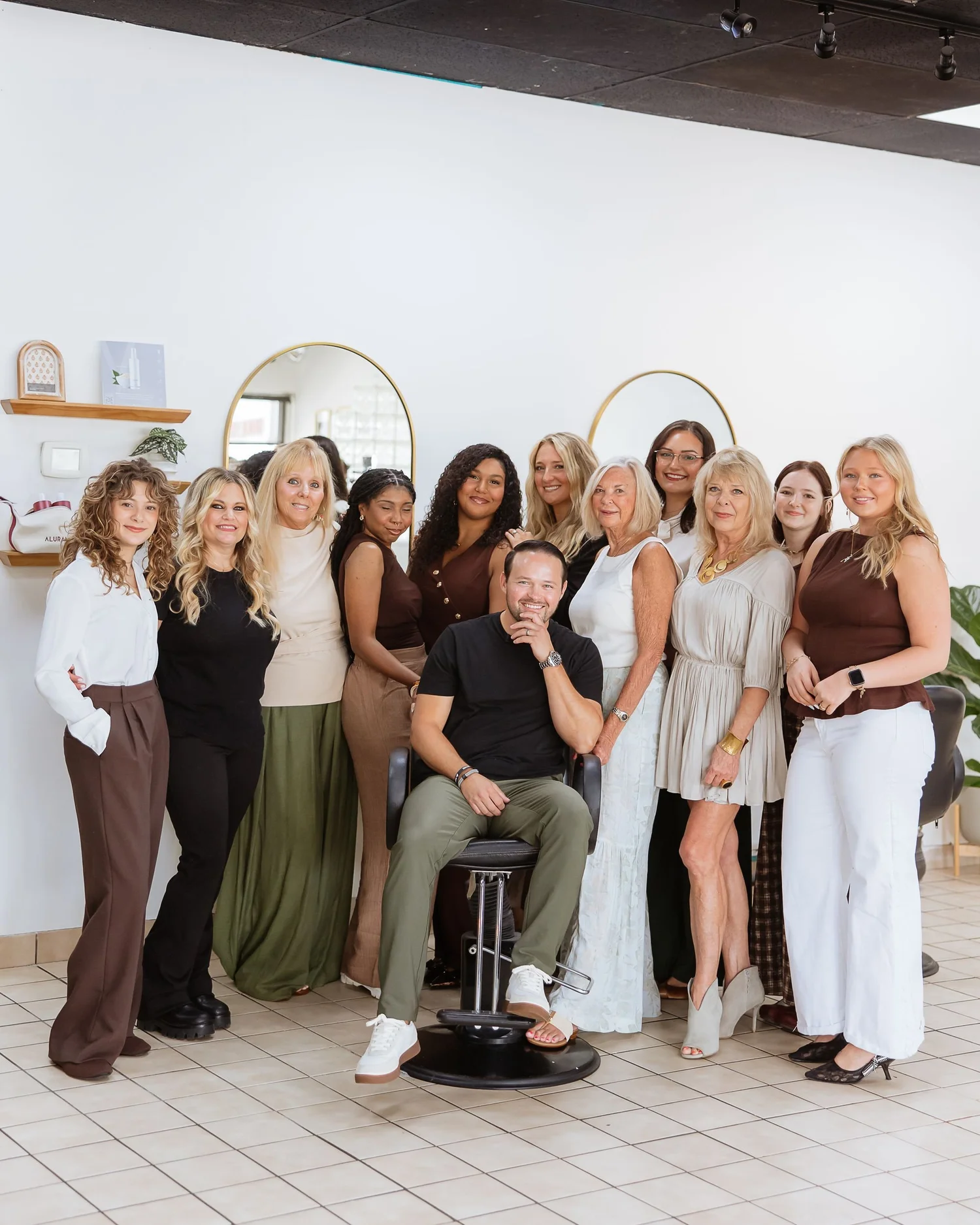 Heads You Win Salon owner Zach seated in a styling chair with the full salon team behind him in the West Ashley salon