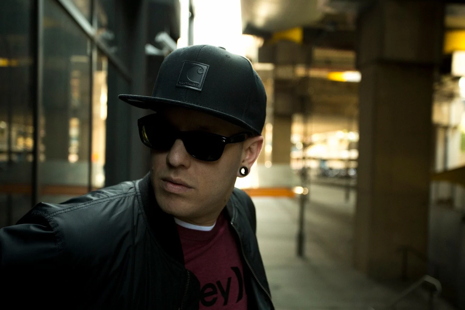 Close portrait of a person wearing a black cap, sunglasses and a dark jacket.