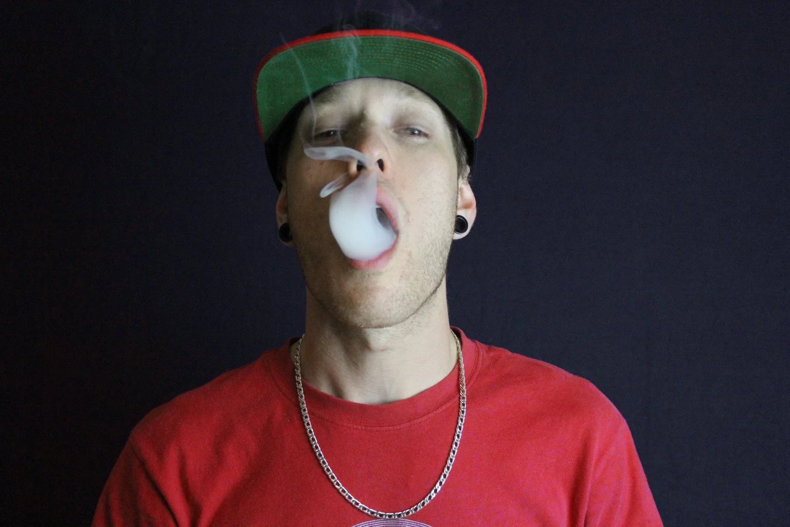 Portrait of a person wearing a red shirt and cap against a dark backdrop.