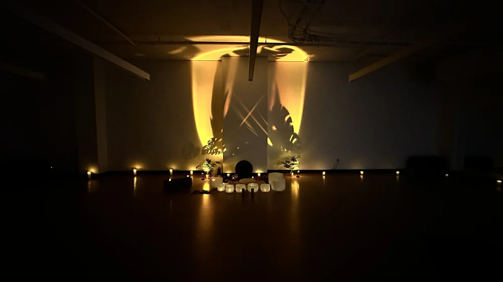 An in-house sound bath for Lululemon: crystal bowls and candlelight before a wall of leaf shadows