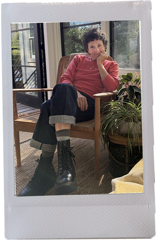 Sarah Rich sitting in a wooden armchair in a sunny room with houseplants