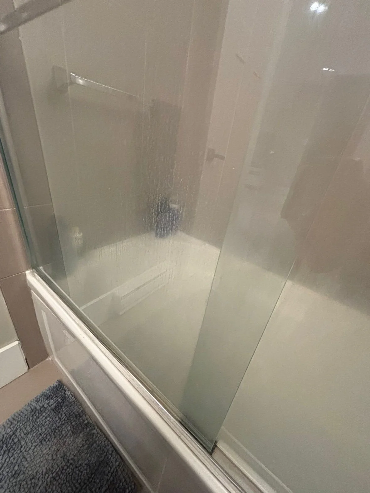 Shower glass door cloudy with soap scum and water spots, before cleaning
