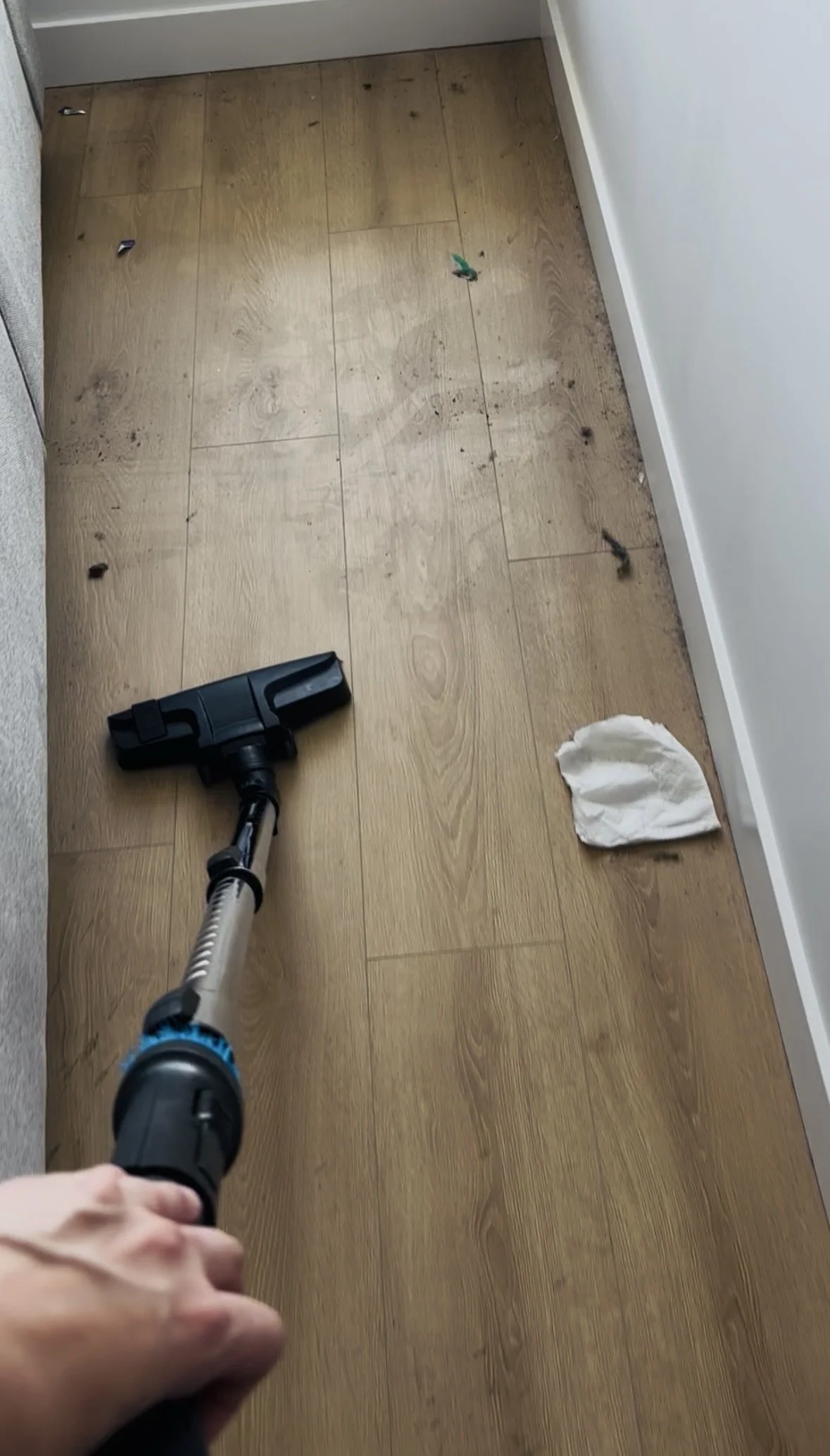 Wood floor covered in dust and debris with vacuum mid-clean, before cleaning