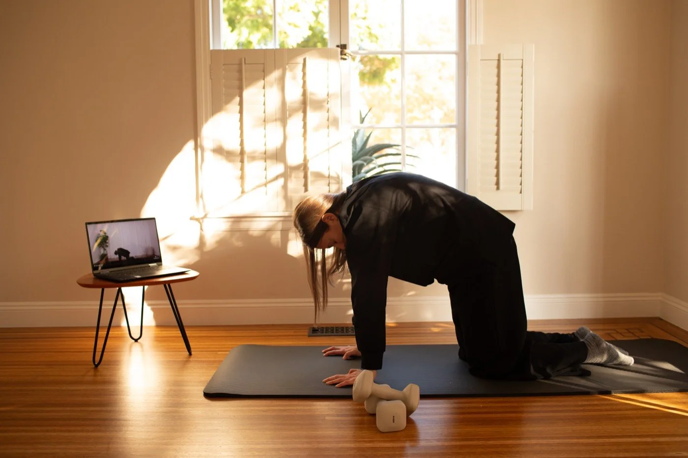 A member in a live Jeem class on her laptop, on all fours on her mat