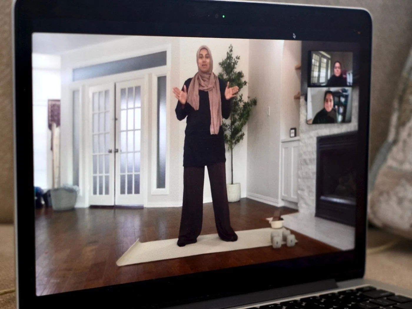 A Jeem instructor in hijab leading a live class on a laptop screen, with members joining on camera