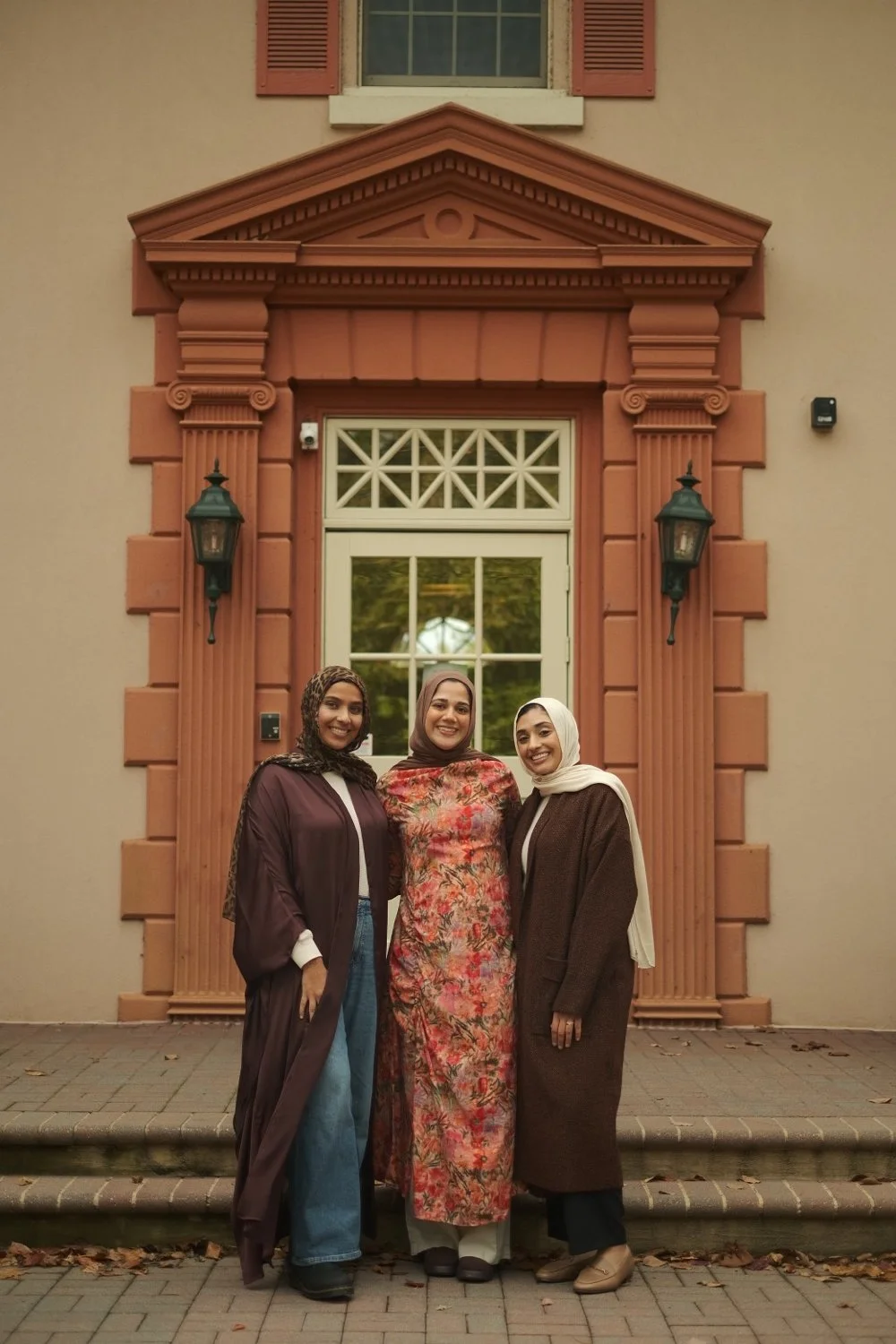 Jeem's three founders, Dhuha, Deena and Sana, standing together in front of a pink doorway