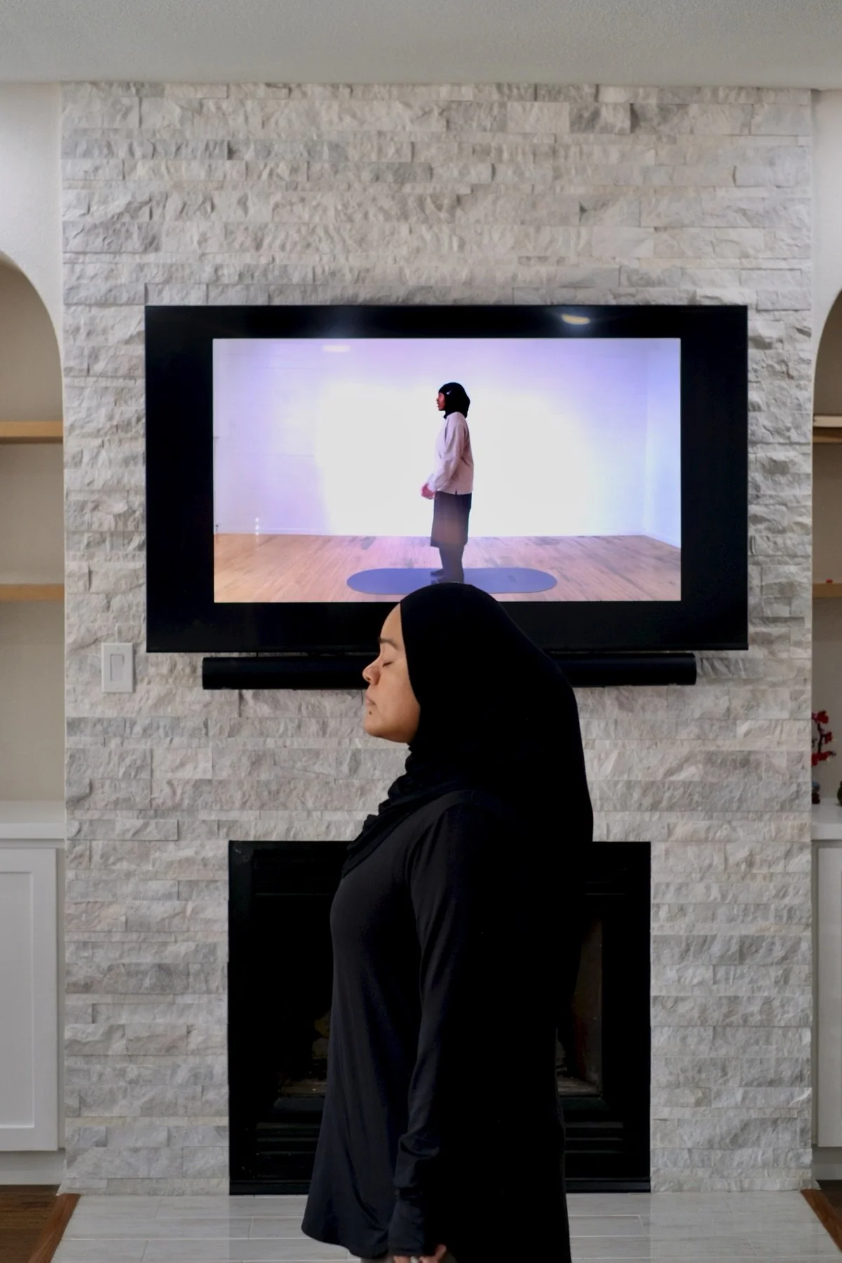 A Jeem member in hijab standing in front of her TV, streaming a Jeem class
