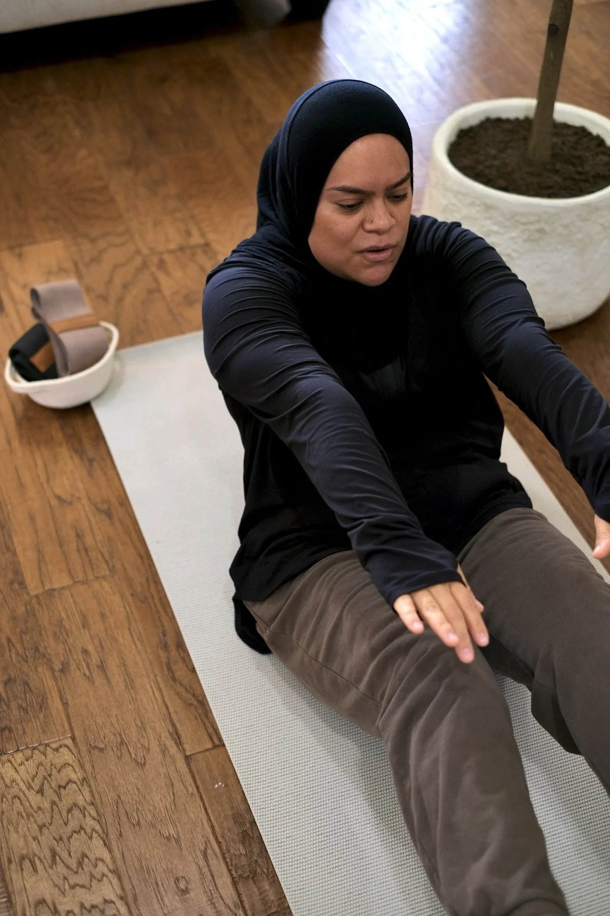 A Jeem member in hijab doing a seated core exercise on her mat