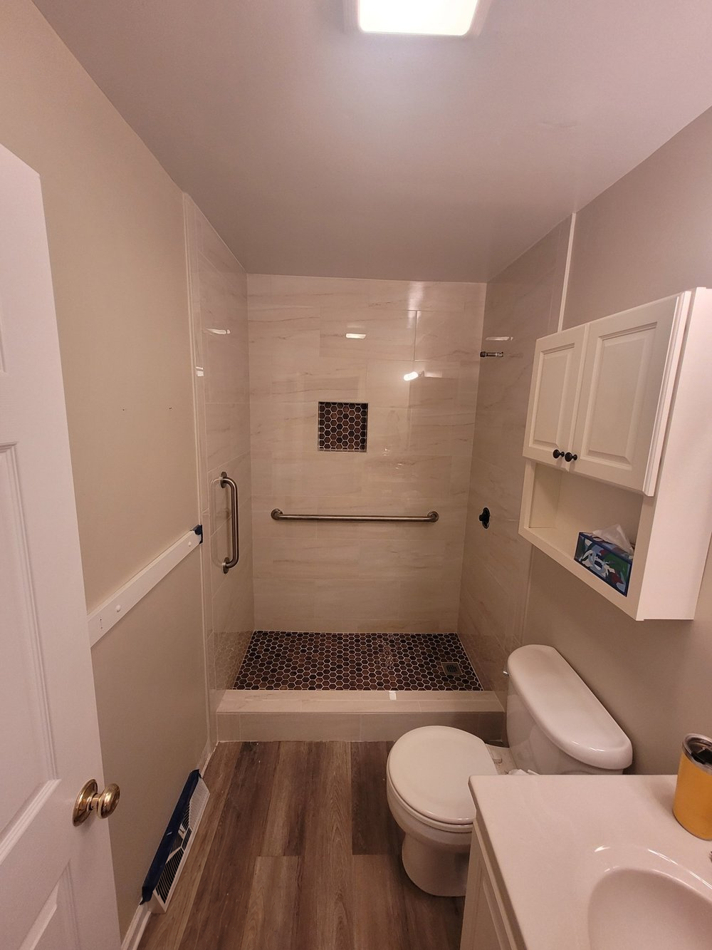 Bathroom with a white tiled shower, recessed niche, toilet, vanity, and wood-look flooring.